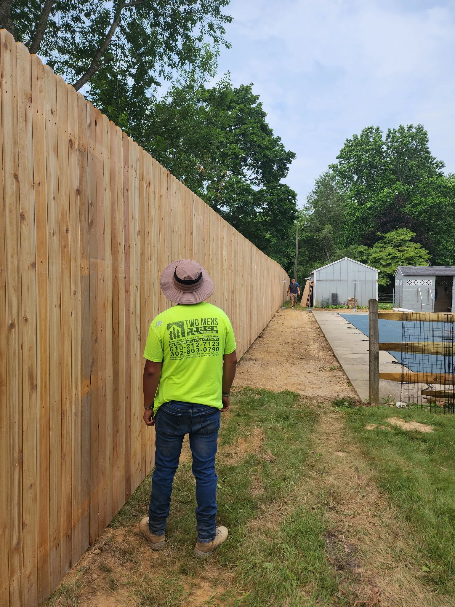 TWOMENS crew member inspecting tall cedar privacy fence installation in Delaware